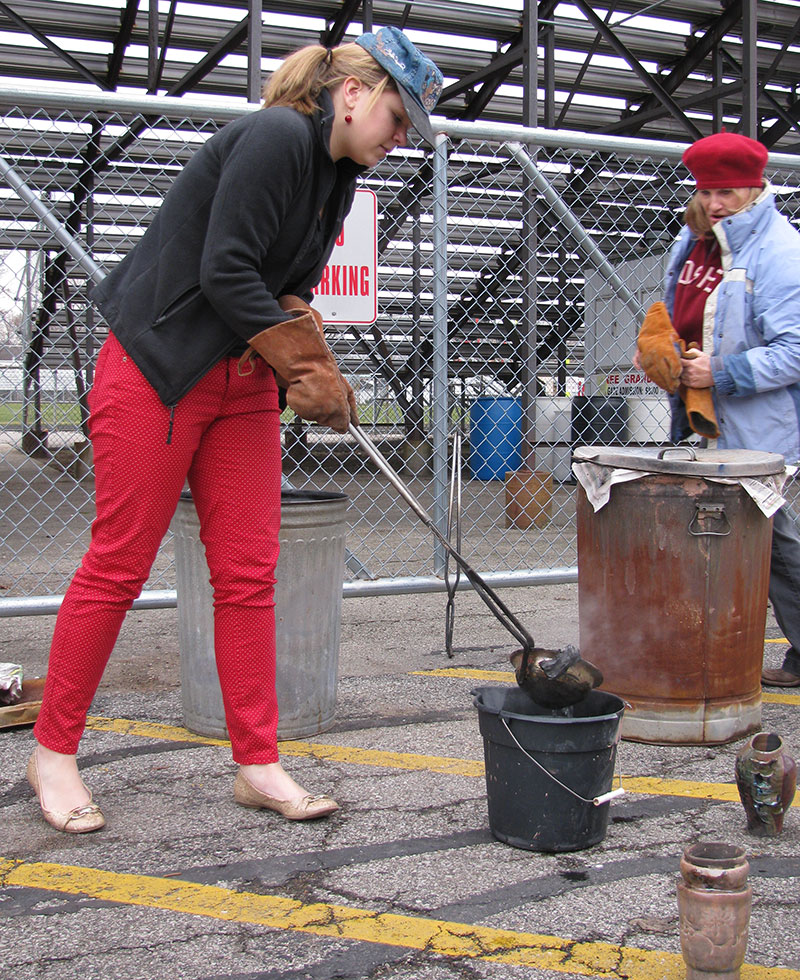 An IB art student places a raku-fired clay piece into water, as teacher Cindy Cooper watches