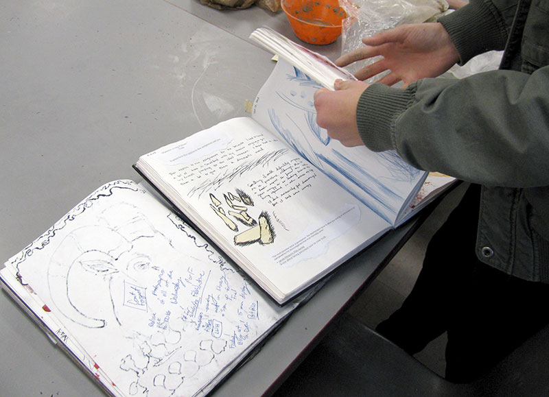 A student flips through her "investigative workbook" for her IB art class. In the investigative workbooks, students create and process ideas.